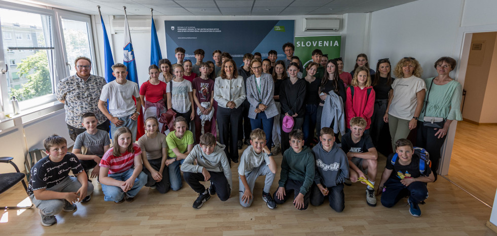 skupina otrok in odraslih stoji v prostoru ob slovenskih zastavah na stalnem predstavništvu Slovenije pri OZN.