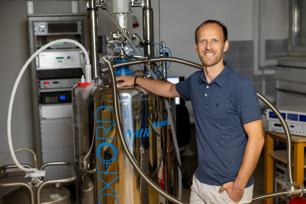 Prof. dr. Andrej Zorko v laboratoriju stoji ob napravi za jedrsko magnetno resonanco in se nasmehne proti kameri.