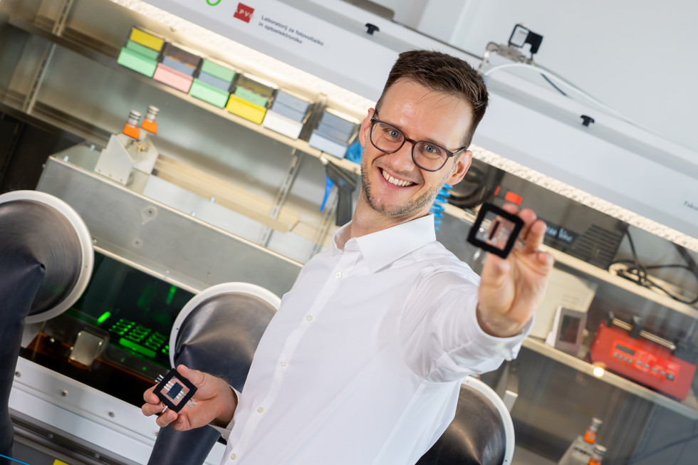 Raziskovalec Marko Jošt v laboratoriju za fotovoltaiko nasmejano drži vzorce sončnih celic iz perovskita.