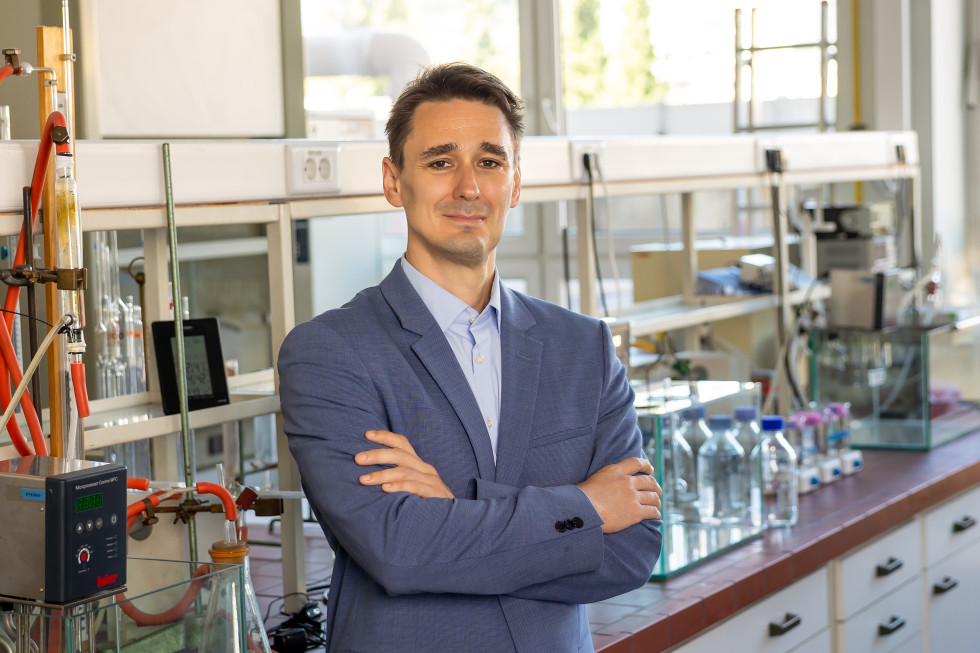 Prof. dr. Urban Bren stoji v laboratoriju s prekrižanimi rokami pred raziskovalno opremo in steklenicami z vzorci.