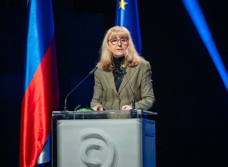Prof. dr. Ljubica Marjanovič Umek med slavnostnim govorom na slovesnosti podelitve Zoisovih nagrad. Stoji za govorniškim pultom, obkrožena z zastavami Slovenije in Evropske unije.