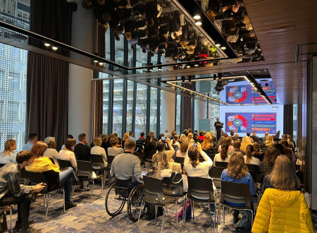 V dvorani sedijo udeleženci konference, gledajo predavatelja.