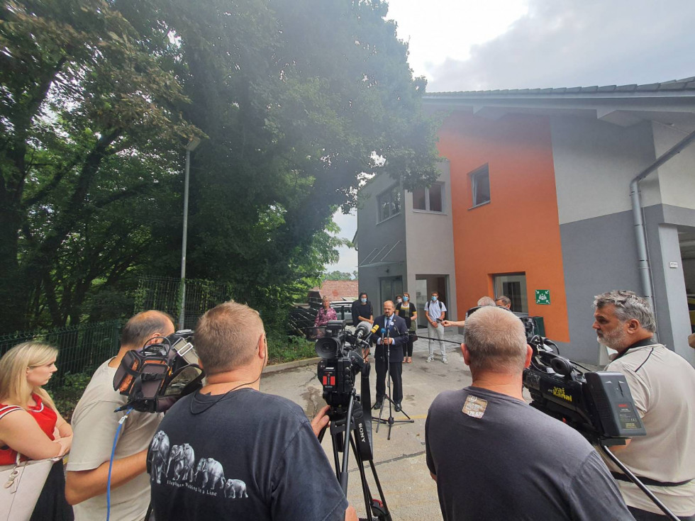 Minister Poklukar pred stavbo daje izjavo, pred njim snemalci in novinarji, v ozadju predstavniki ZD Metlika