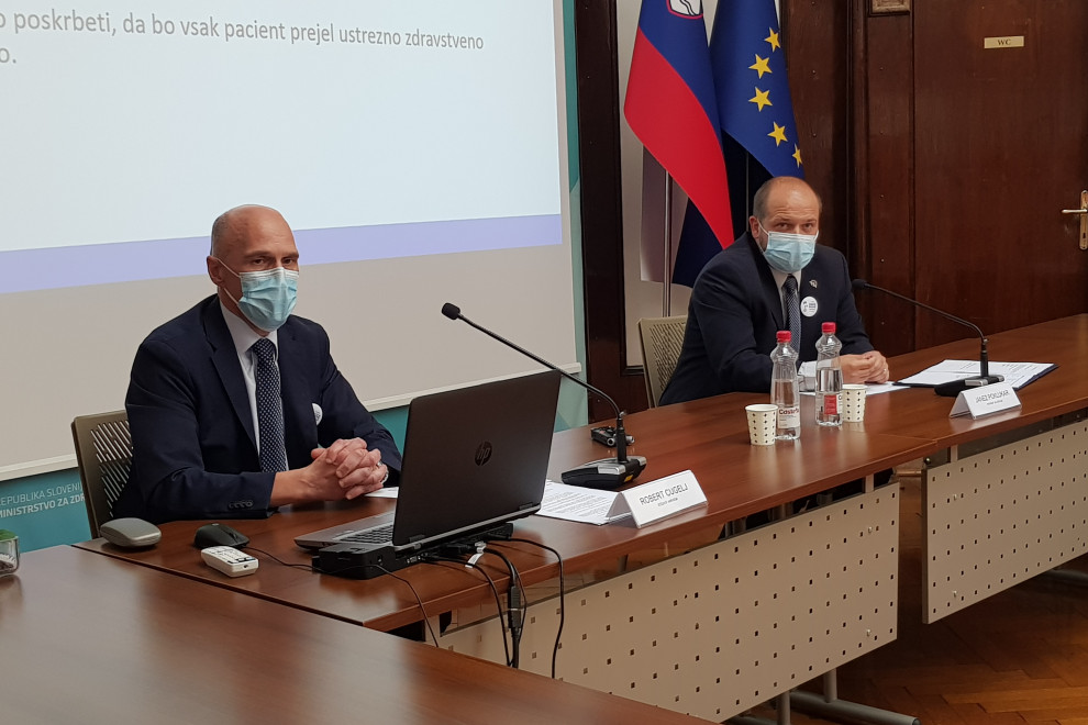 Državni sekretar in minister za konferenčno mizo, v ozadju zastavi Slovenije in EU.