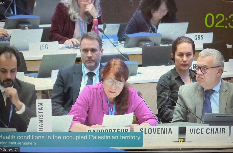 Zasedanje Svetovne zdravstvene organizacije, v vrstah belih miz sedijo ljudje, pred njimi so mikrofoni, v ospredju je ženska v vijoličasti majici, pred njo je napis Slovenija. Ženska bere z lista.