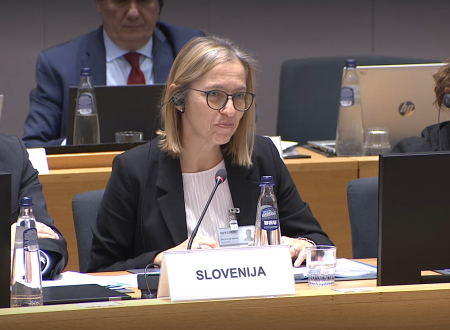 Ministrica za zdravje kot predstavnica Slovenije sedi in govori v namizni mikrofon
