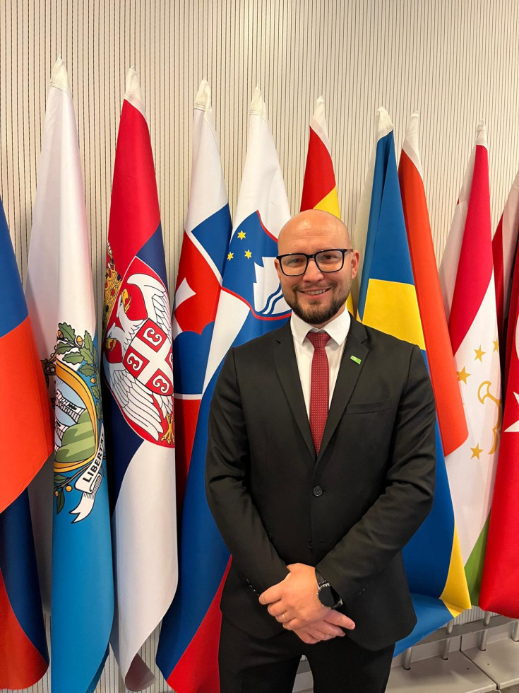 Moški stoji pred zastavami v poslovni obleki