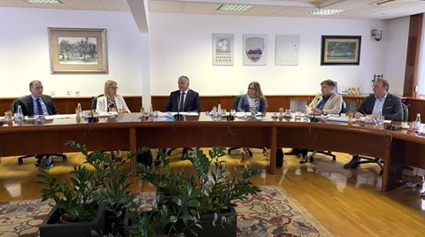 Ministrica v belem suknjiču sedi za veliko ovalno mizo iz mahagonja, ob njej sedijo predstavniki združenja