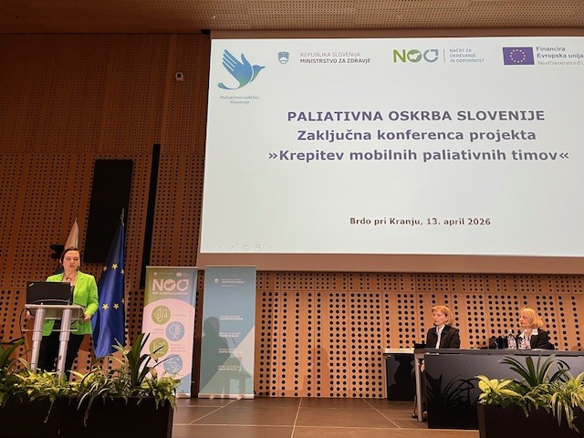 Državna sekretarka stoji za govorniškim pultom in nagovarja udeležence