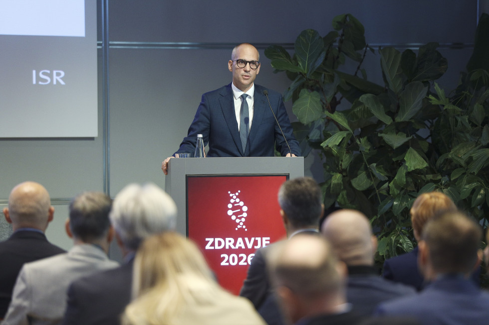 Minister na odru za govorniškim pultom, pred njim je občinstvo
