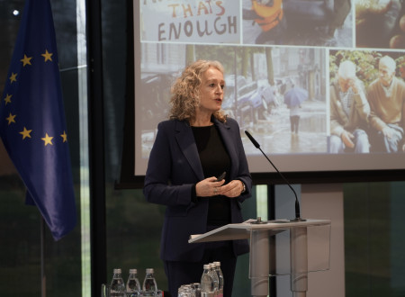 Ženska v črni obleki stoji pred mikrofonom na govorniškem pultu