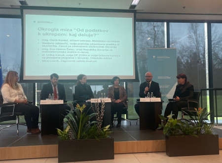 Udeleženci sedijo v polkrogu, za njimi diapozitiv z imeni udeležencev