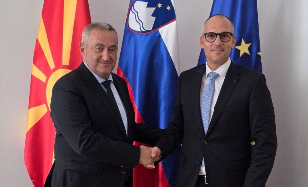 Ministra v temnih moških oblekah stojita pred makedonsko, slovensko in evropsko zastavo in se rokujeta