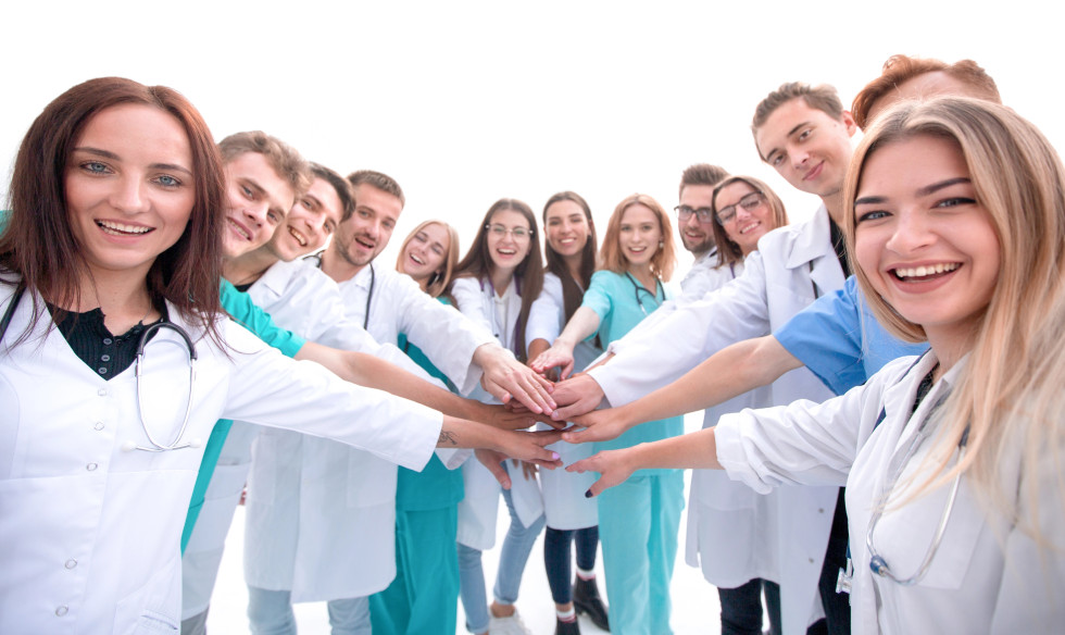 Mlade ženske in moški držijo iztegnjeno roko, se dotikajo in tako tvorijo polkrog. Njihovi obrazi so nasmejani.