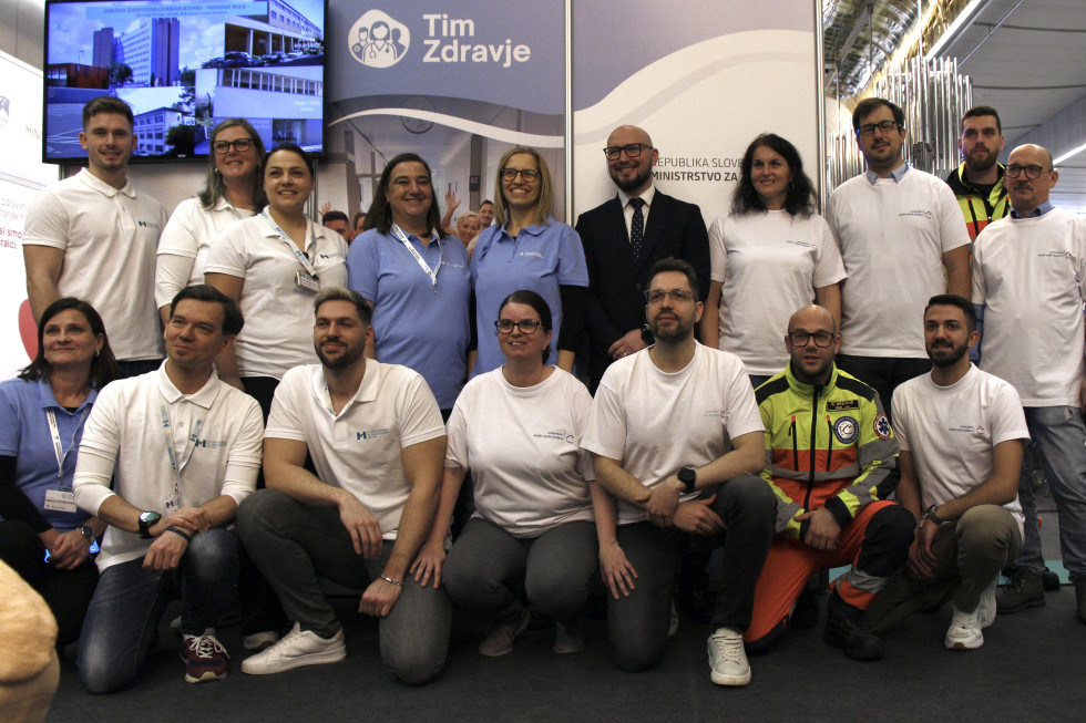 Skupina se slika pred znakom ministrstva za zdravje kot del kampanje Tim zdravje