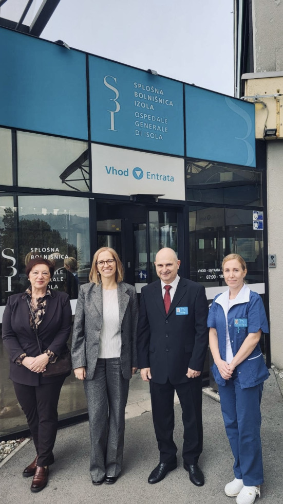 Ministrica pred stavbo bolnice z vodstvom. 