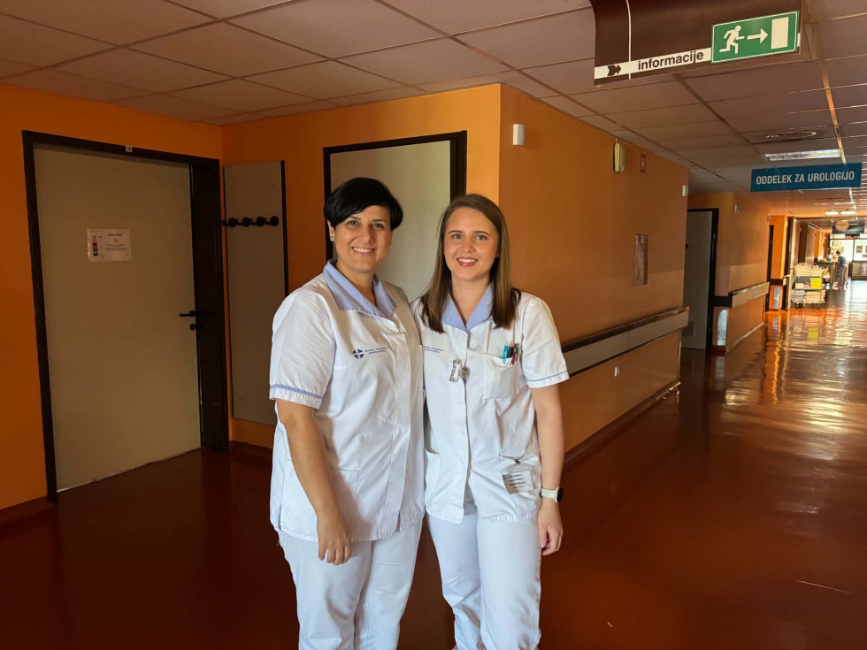 Nasmejani medicinski sestri v uniformah pozirata na hodniku bolnišnice.