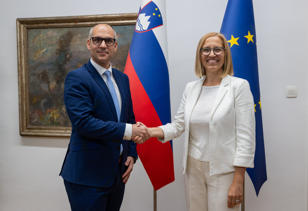 Novi minister in odhajajoča ministrica za zdravje, ki se rokujeta v sejni sobi pred slovensko in EU zastavo