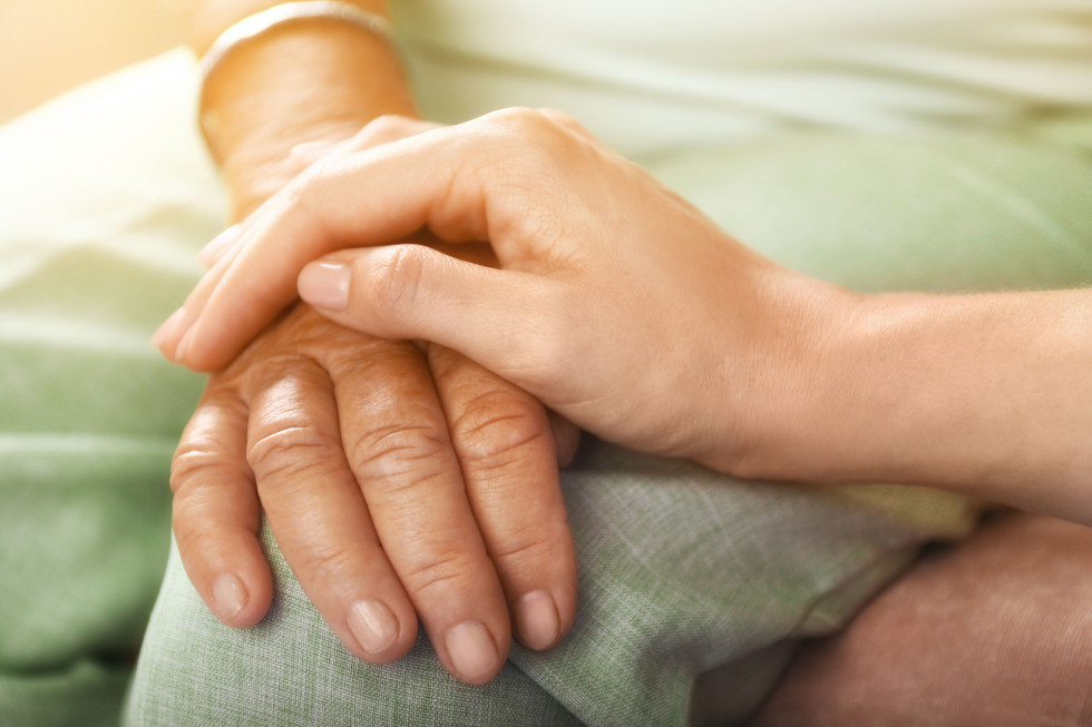 Roka mlajše ženske, ki drži roko starejše ženske.