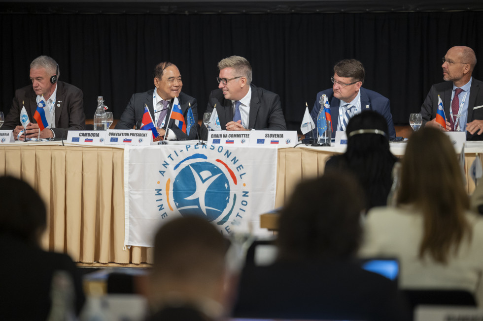 državni sekretar med konferenco sedi z ostalimi govorci za osrednjim omizjem