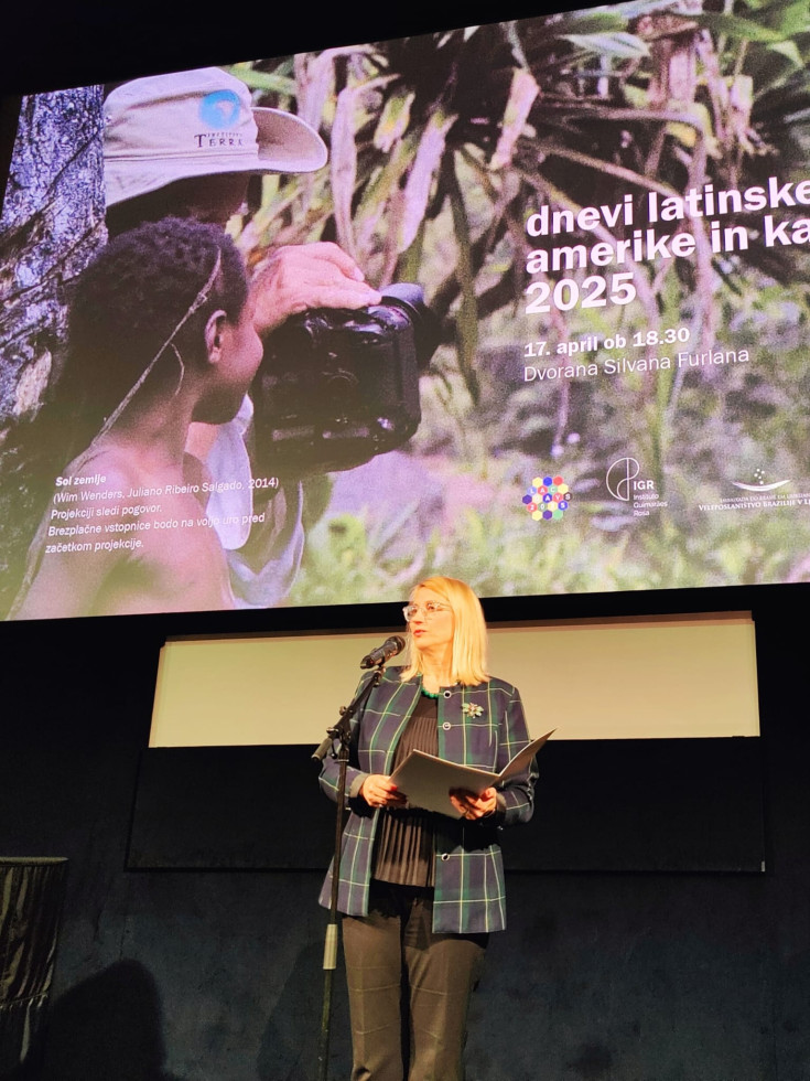 Ženska stoji pred filmskim platnom in govori