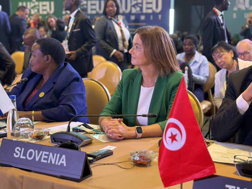 Ministrica sedi za mizo, pred njo napis Slovenija