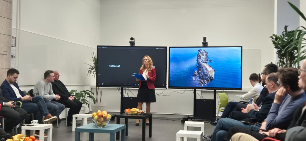 A woman is standing and speaking in front of screens.
