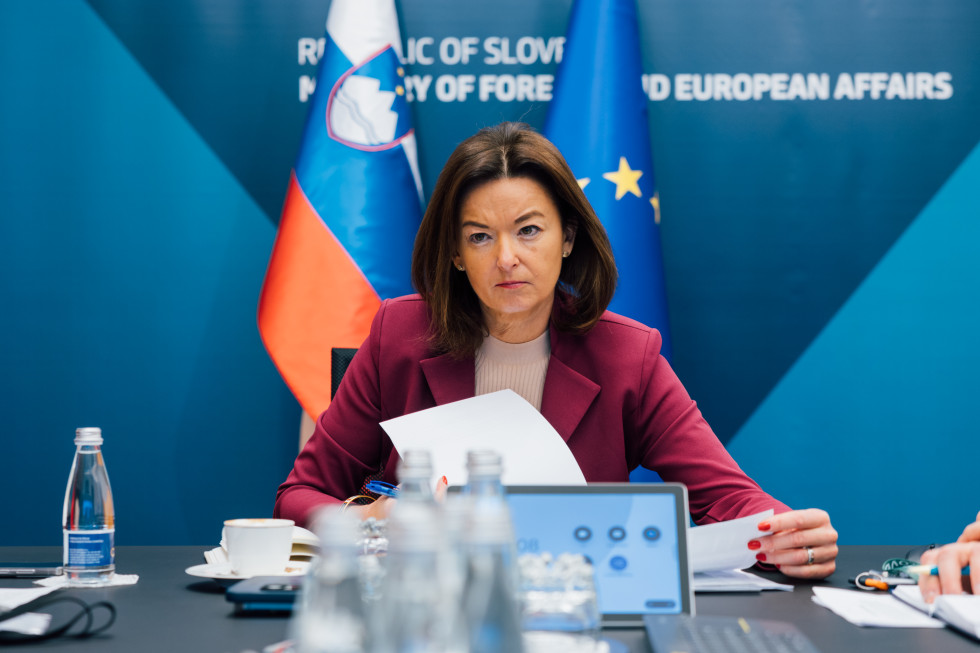 ministrica sedi in posluša virtualno ministrsko srečanje