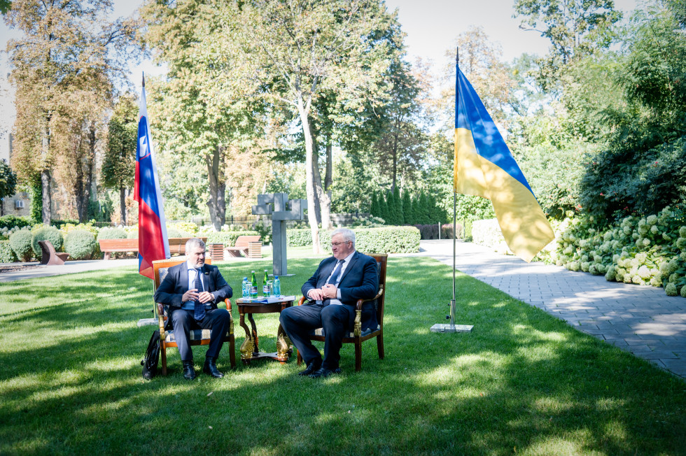 Kajzer in Sibiha sedita na travi, v ozadju sedijo zastave