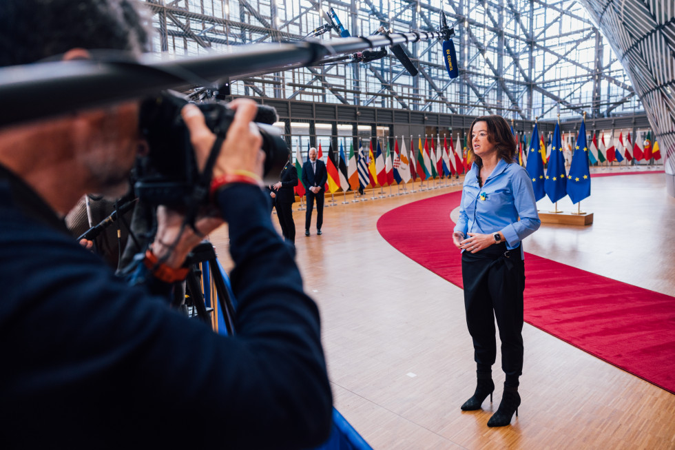 Minister in front of cameras and microphones, with flags behind her