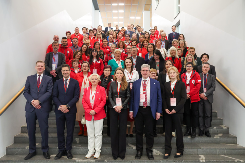 Velika skupina ljudi, večinoma v rdečih majicah, pozira za skupinsko fotografijo v notranjem prostoru.