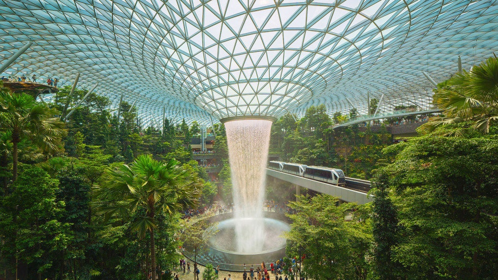 indoor jungle with a waterfall flowing from a circular opening in the glass roof