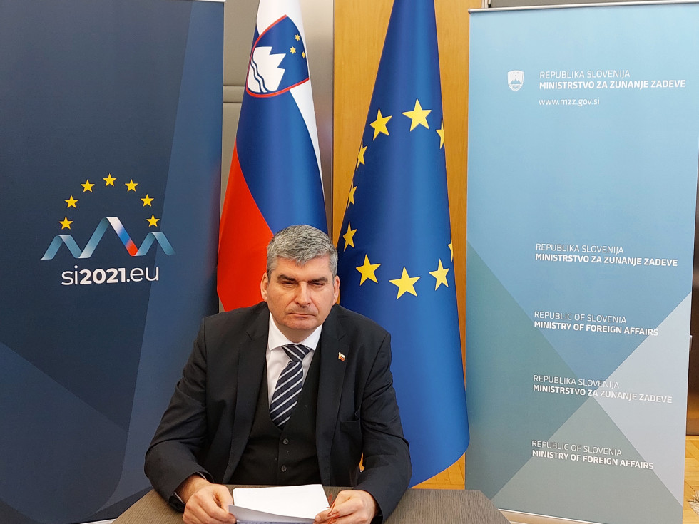 state secretary Raščan sitting at the table, flags behind him