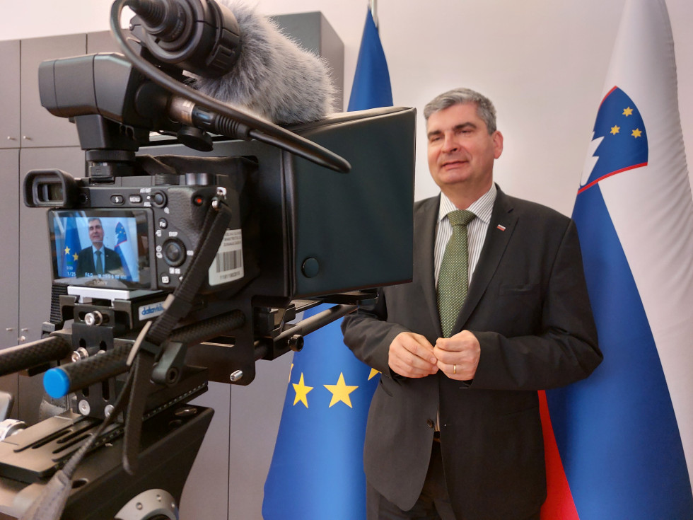 state secretary in front of the camera, flags behind him