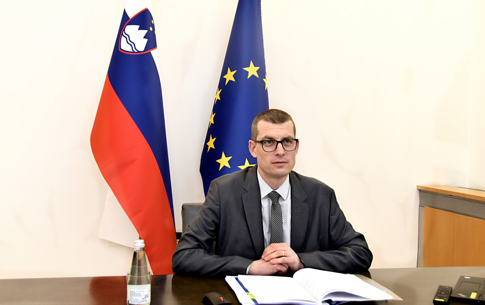 State Secretary sitting in front of computer with flags in behind