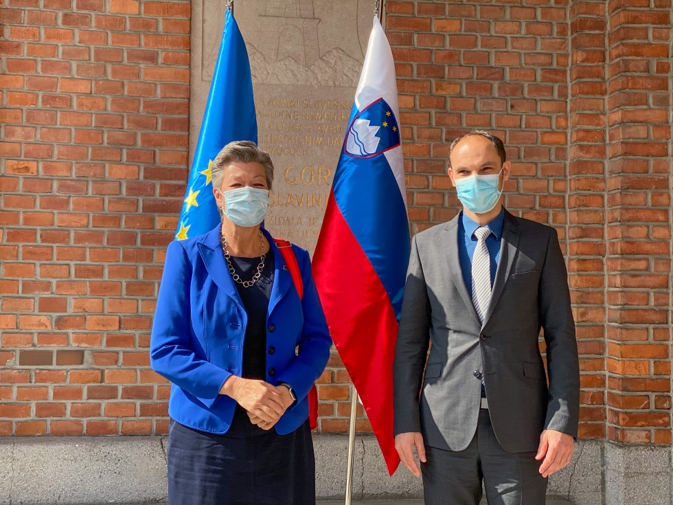 Minister and Commissioner are standing in front of the flags outside the building