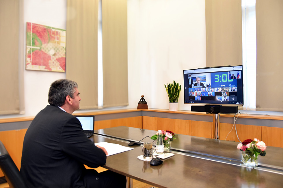 državni sekretar sedi za mizo, ekran z udeleženci