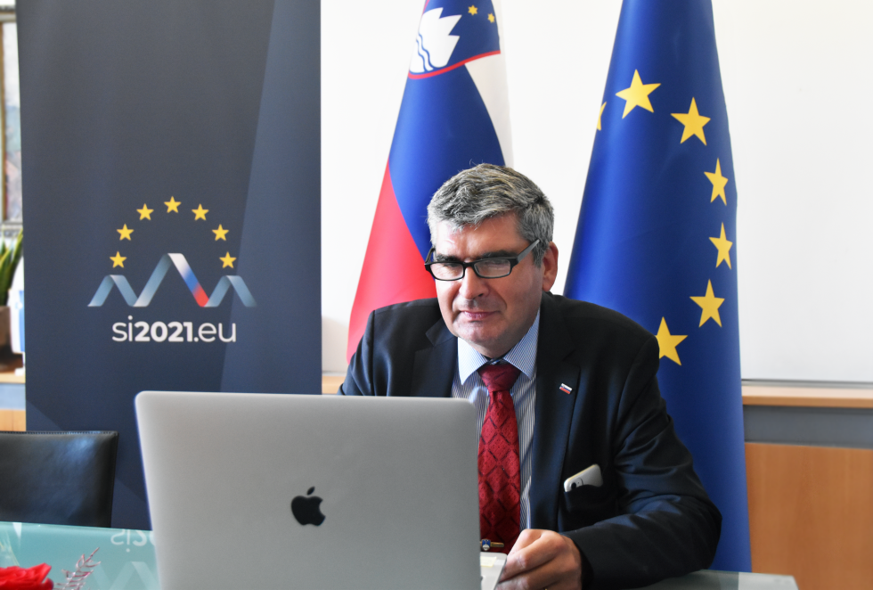 sekretar pred zaslonom, v ozadju zastavi Slovenije in EU