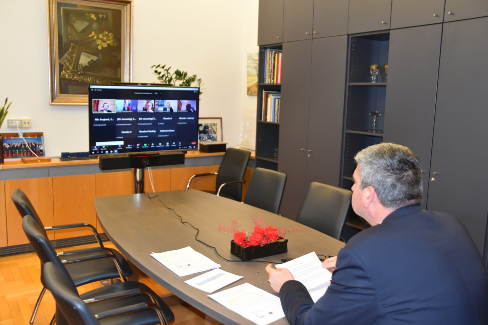 državni sekretar Raščan sedi za mizo, gleda v ekran