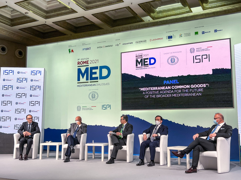 Panelisti med panelno razpravo sedijo na odru v ozadju logotip konference