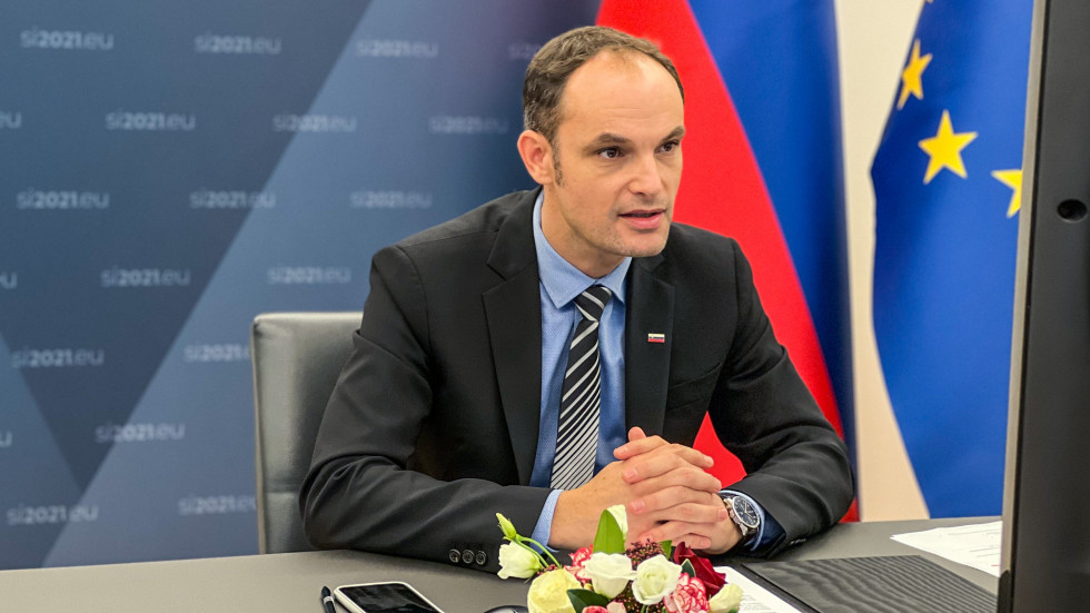 minister Anže Logar sedi za mizo, govori preko AVK