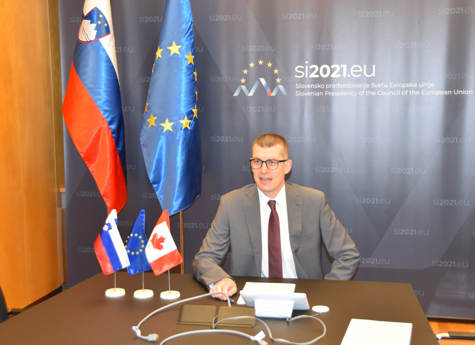 državni sekretar Dovžan sedi za mizo, v ozadju pano Eu2021Si in zastave