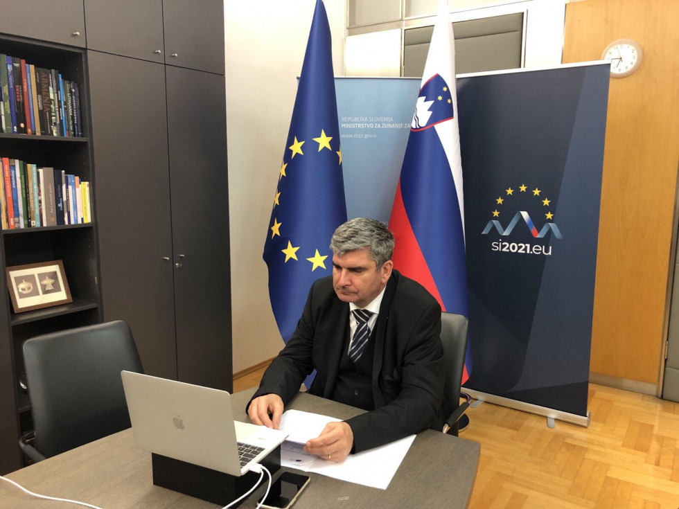 Državni sekretar med avdio-video konferenco, v ozadju zastavi Slovenije in EU