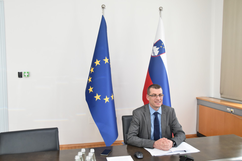 State Secretary Gašper Dovžan sittin at the table infront of flags