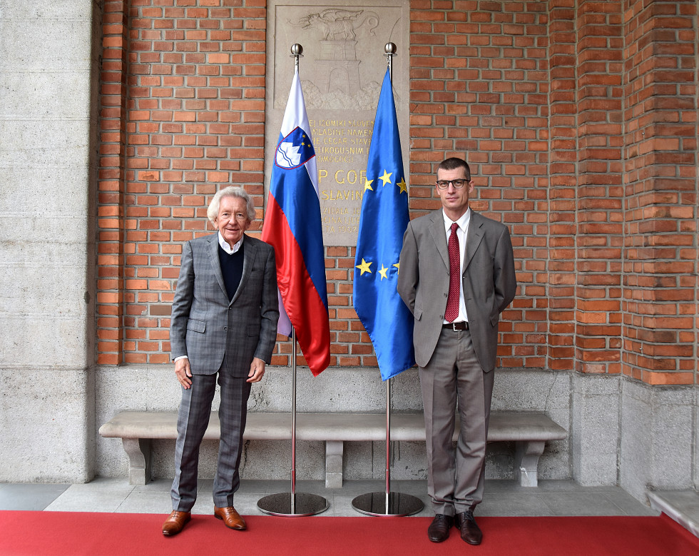 State Secretary Gašper Dovžan stands infront of flags with Stephan Holthoff-Pförtner