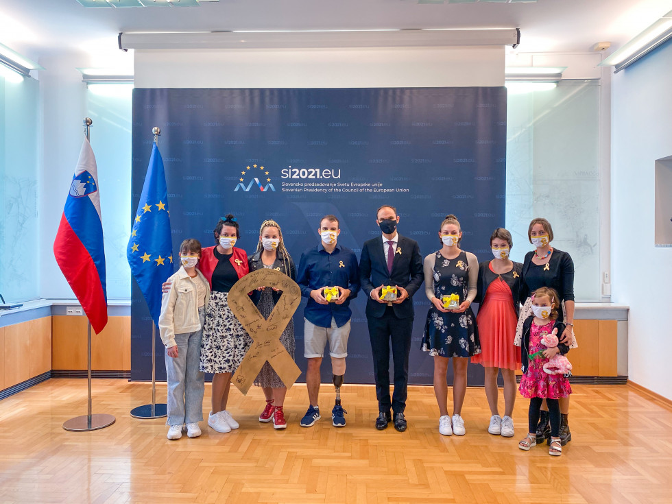 Člani ekipe z ministrom pred ozadjem z logotipom slovenskega predsedovanja Svetu EU, v rokah držijo zlate pentljice, ob strani stojita slovenska in evropska zastava