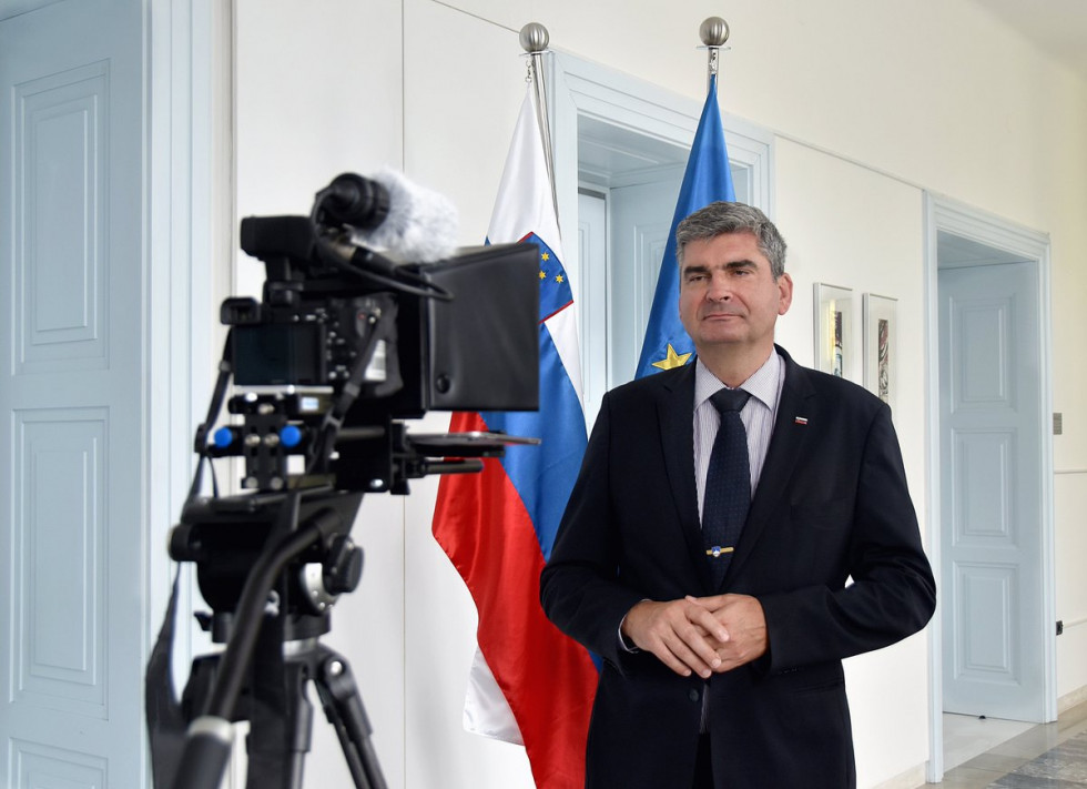 State Secretary dr. Raščan stands in front of the teleprompter with which his address is being recorded, Slovenian and European flags in the background
