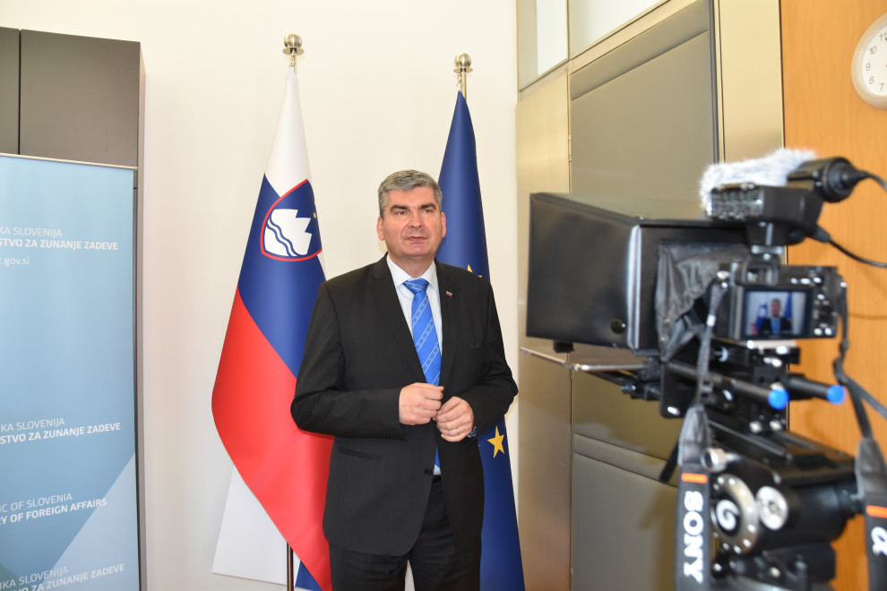 State Secretary Raščan infront of camera, flags behind
