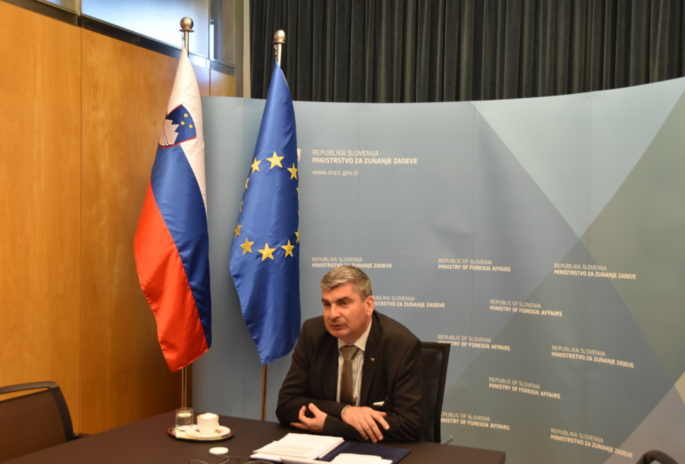State Secretary Raščan sits at the table, behing him Slovenian and EU flag