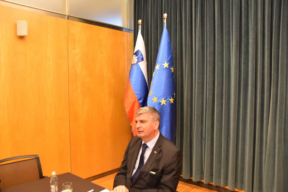 državni sekretar Raščan sedi v pisarni, za njim slovenska in evropska zastava
